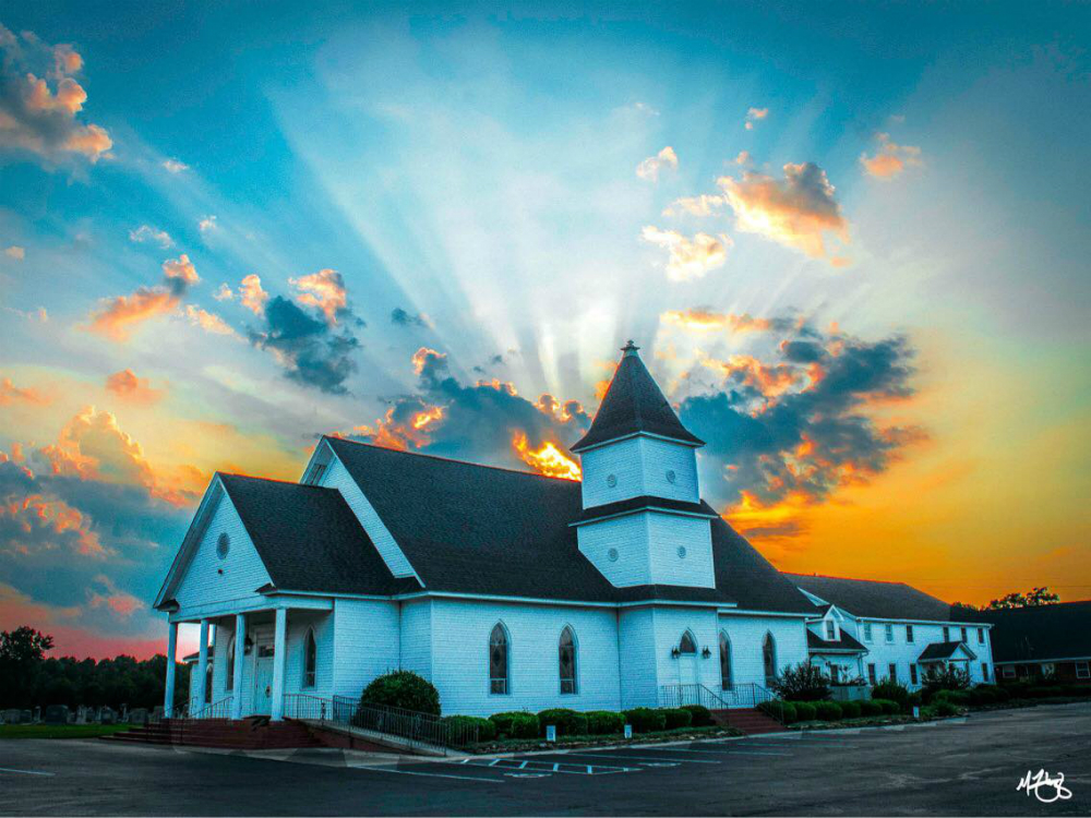 White church with a gray roof and a sunset of the sky